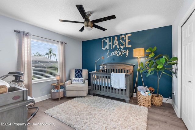 bedroom with a closet, a nursery area, hardwood / wood-style flooring, and ceiling fan