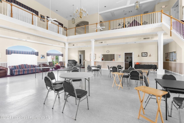 dining room with a towering ceiling, ceiling fan with notable chandelier, and ornate columns