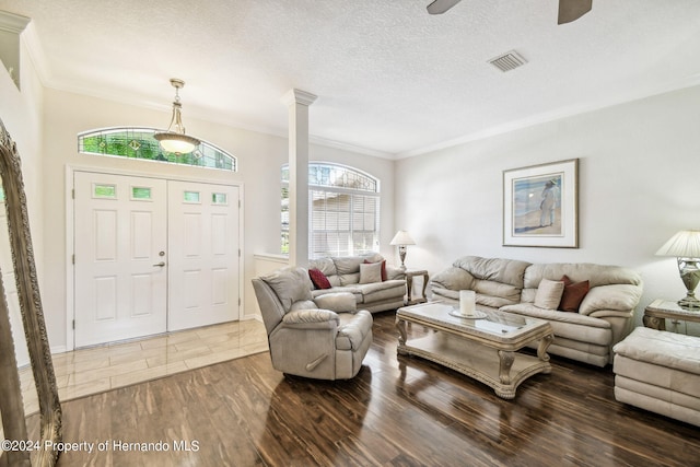 living room featuring dark wood-type flooring, ceiling fan, crown molding, and decorative columns