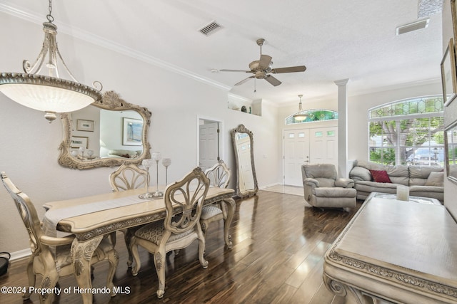 dining room featuring ceiling fan, a textured ceiling, crown molding, dark wood-type flooring, and ornate columns