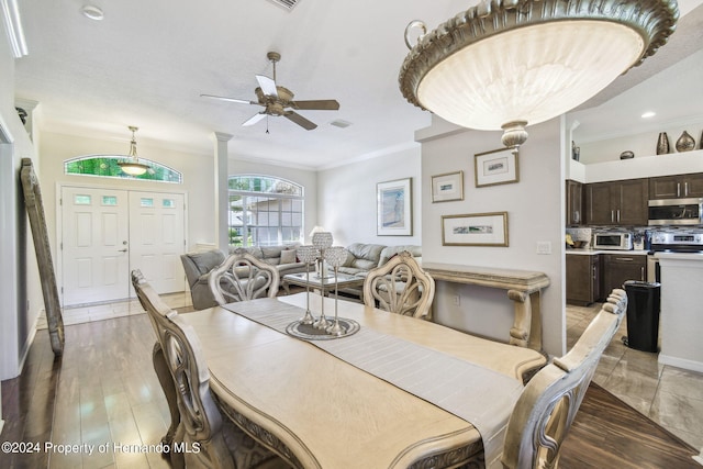 dining space featuring ceiling fan, ornate columns, light wood-type flooring, and ornamental molding