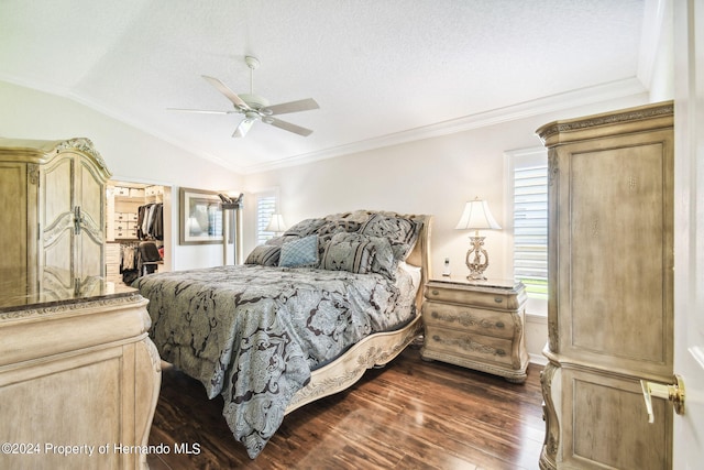 bedroom with vaulted ceiling, ornamental molding, dark hardwood / wood-style floors, ceiling fan, and a walk in closet