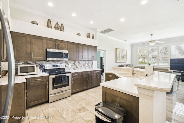 kitchen featuring a center island with sink, dark brown cabinetry, sink, crown molding, and appliances with stainless steel finishes