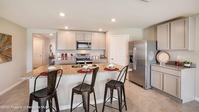 kitchen with light stone counters, a breakfast bar area, an island with sink, gray cabinetry, and appliances with stainless steel finishes