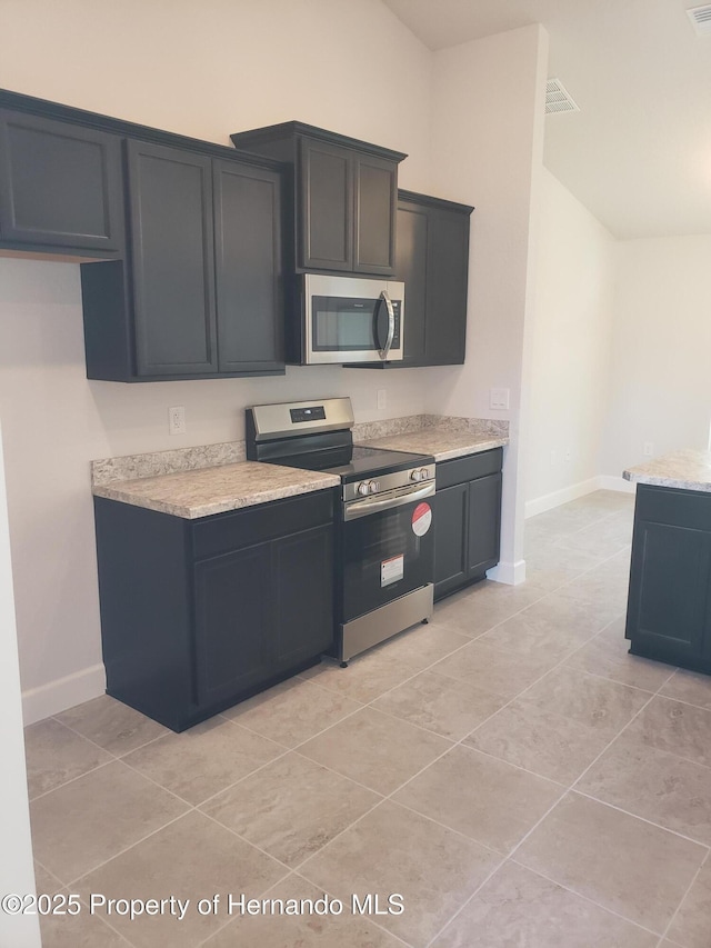 kitchen featuring baseboards, appliances with stainless steel finishes, light stone counters, and dark cabinets