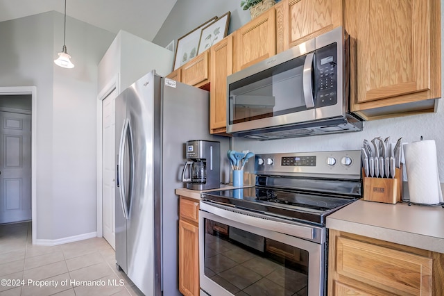 kitchen featuring appliances with stainless steel finishes, hanging light fixtures, light tile patterned floors, and vaulted ceiling