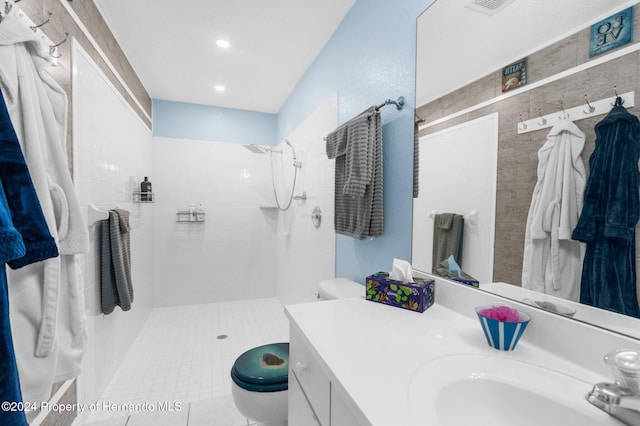 bathroom with vanity, tiled shower, tile patterned floors, toilet, and tile walls