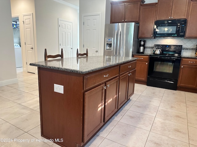 kitchen with light tile patterned flooring, black appliances, ornamental molding, dark stone counters, and a kitchen island with sink