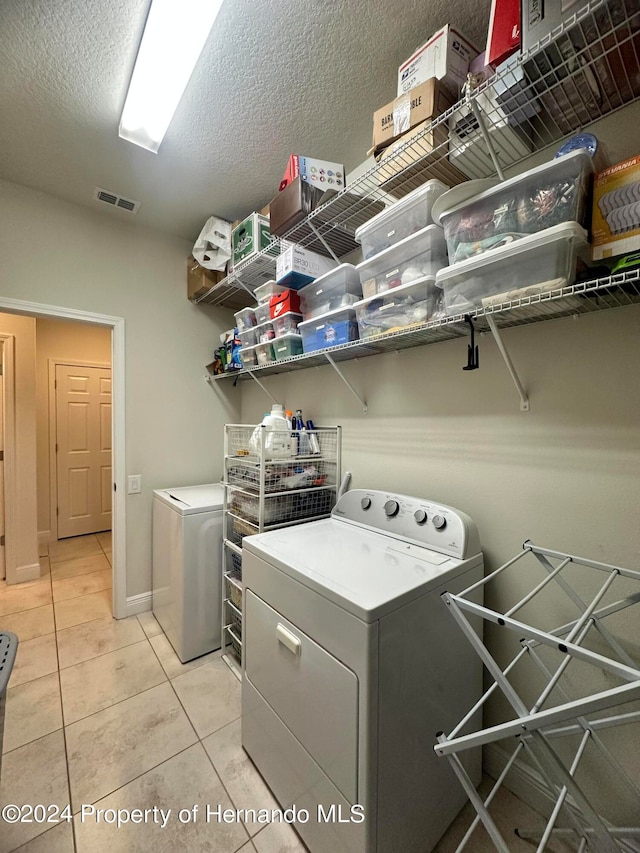 washroom with washing machine and dryer, a textured ceiling, and light tile patterned floors