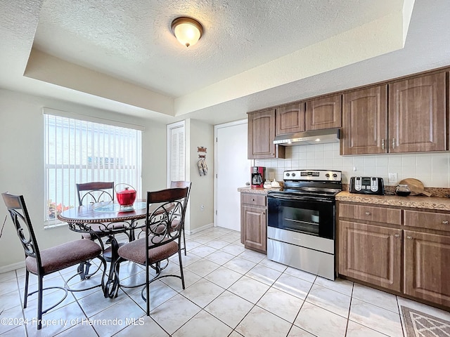 kitchen featuring stainless steel range with electric cooktop, light tile patterned flooring, a textured ceiling, a raised ceiling, and decorative backsplash