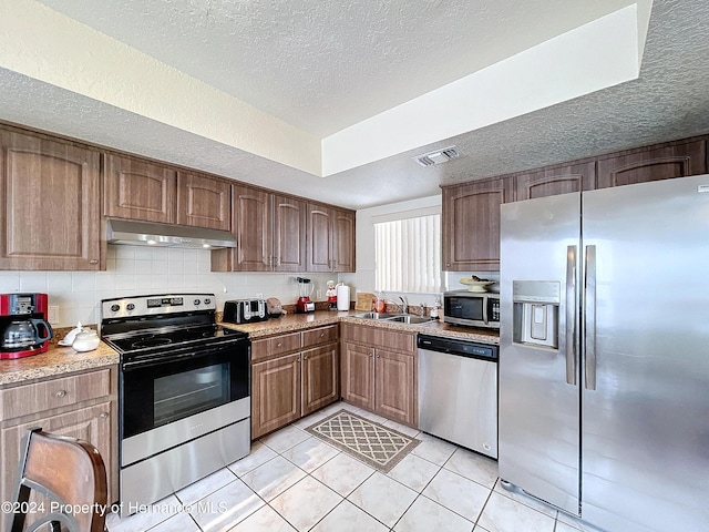 kitchen featuring appliances with stainless steel finishes, a textured ceiling, light tile patterned floors, exhaust hood, and decorative backsplash