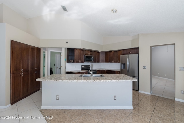 kitchen with a kitchen island with sink, vaulted ceiling, dark brown cabinets, and stainless steel appliances