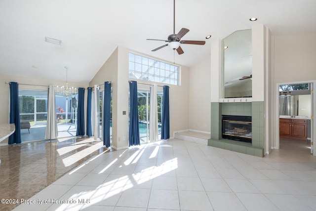 unfurnished living room featuring a high ceiling, a tiled fireplace, light tile patterned floors, and ceiling fan with notable chandelier