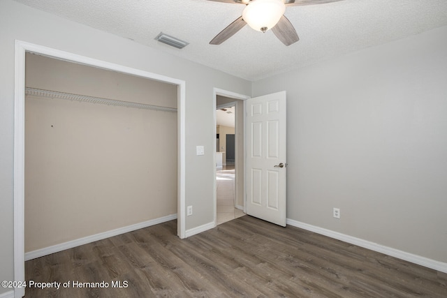 unfurnished bedroom with a closet, ceiling fan, a textured ceiling, and dark hardwood / wood-style floors