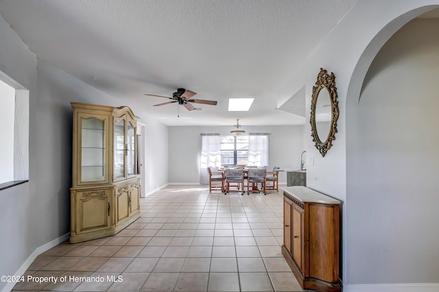 interior space featuring a skylight, light tile patterned floors, and ceiling fan