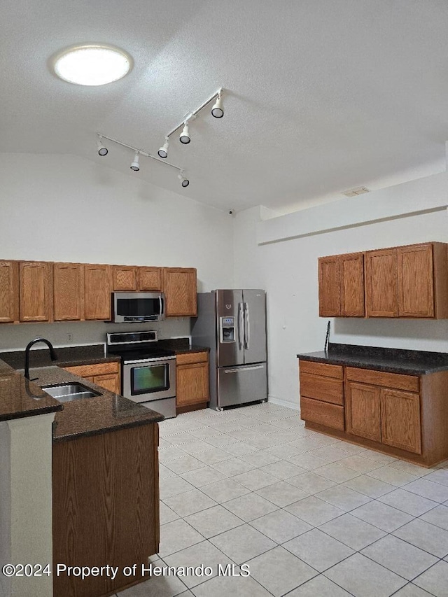 kitchen with stainless steel appliances, light tile patterned flooring, sink, a textured ceiling, and lofted ceiling