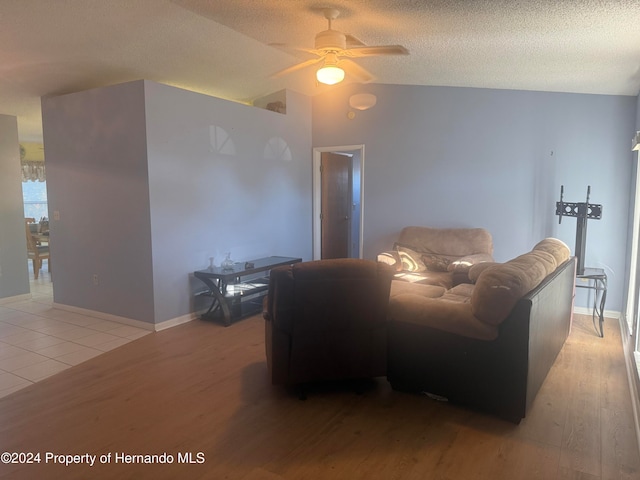 living room with light hardwood / wood-style floors, a textured ceiling, ceiling fan, and vaulted ceiling