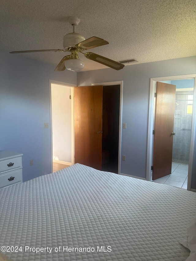 unfurnished bedroom with ceiling fan, a textured ceiling, a walk in closet, connected bathroom, and a closet