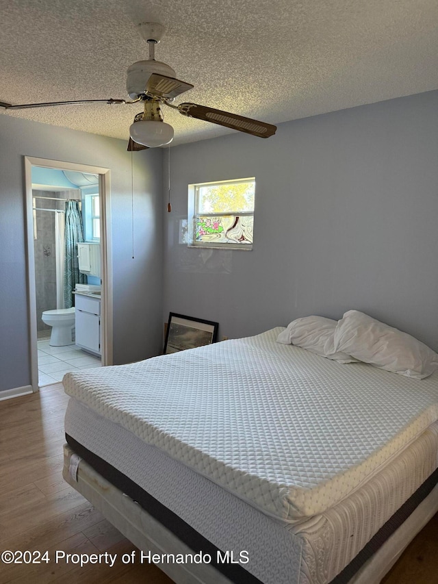 bedroom with ceiling fan, a textured ceiling, light hardwood / wood-style floors, and ensuite bath