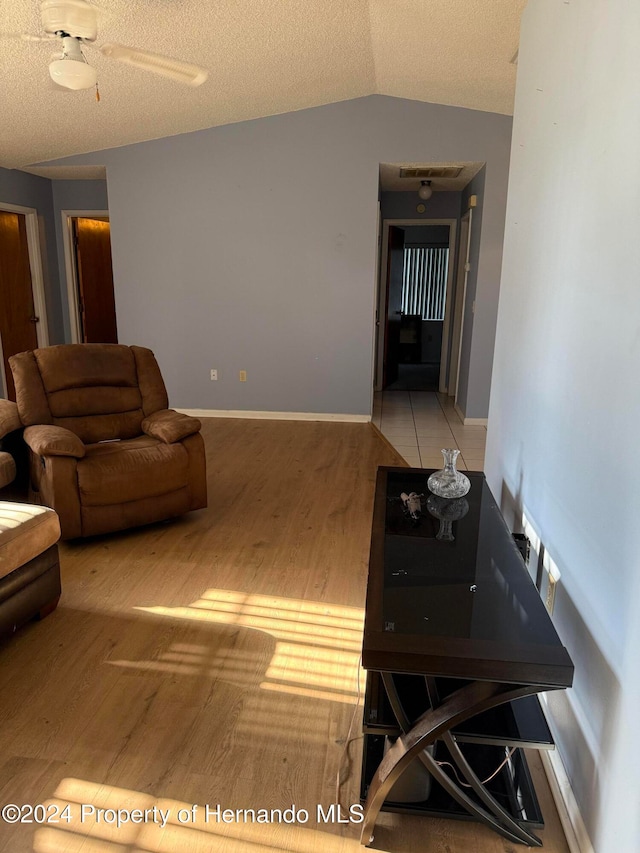 living room featuring light hardwood / wood-style floors, ceiling fan, a textured ceiling, and lofted ceiling