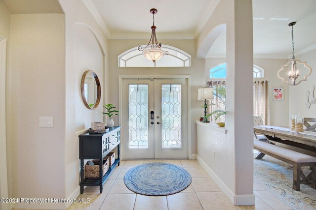 tiled foyer entrance with french doors, crown molding, and a notable chandelier