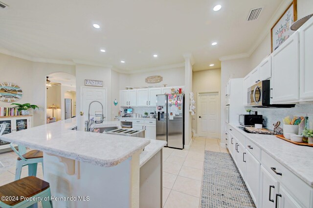 kitchen featuring a center island with sink, white cabinets, a breakfast bar area, tasteful backsplash, and stainless steel appliances