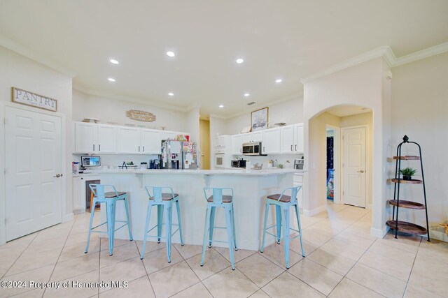 kitchen with a breakfast bar, a center island with sink, white cabinets, ornamental molding, and stainless steel appliances