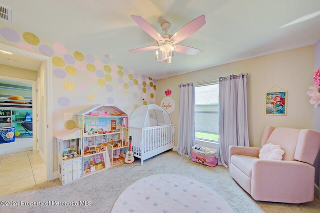 bedroom featuring a crib, light colored carpet, and ceiling fan