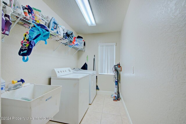 laundry area with a textured ceiling, light tile patterned flooring, separate washer and dryer, and sink