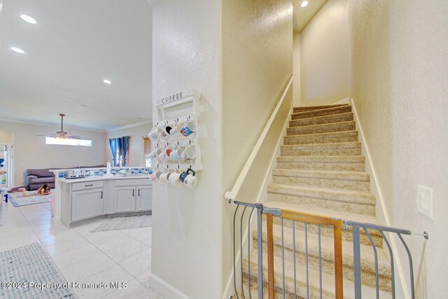 staircase with tile patterned floors, ceiling fan, and ornamental molding