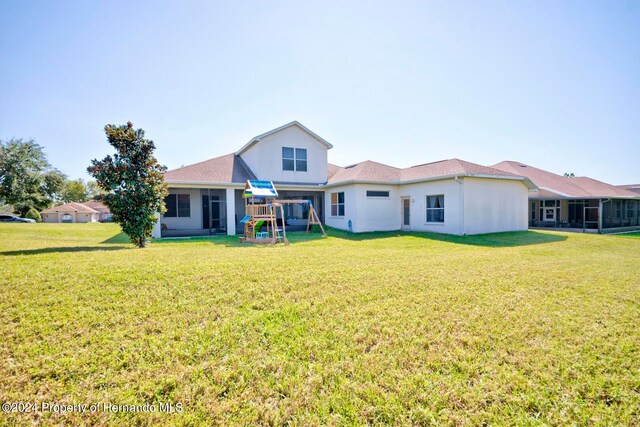 rear view of property featuring a playground and a yard