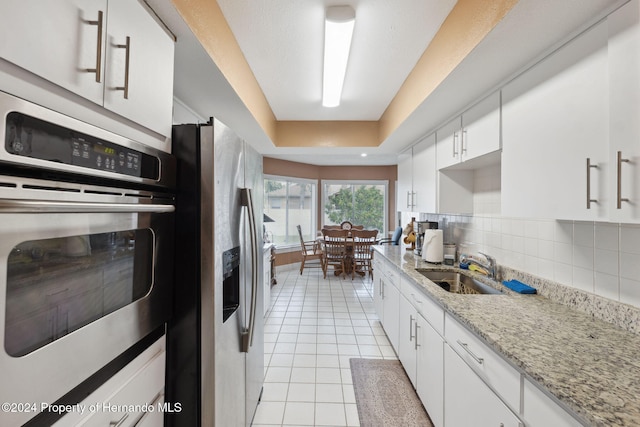 8227 Rhanbuoy Rd, Spring Hill, FL 34606 - kitchen with appliances with stainless steel finishes, light tile patterned floors, white cabinets, tasteful backsplash, and light stone counters