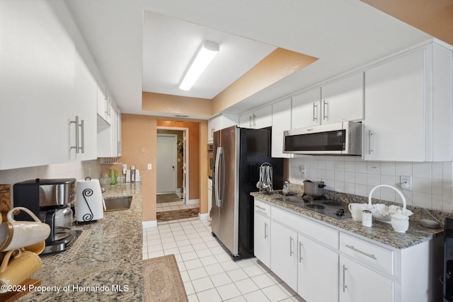 kitchen featuring stainless steel appliances, light tile patterned flooring, white cabinetry, dark stone counters, and backsplash