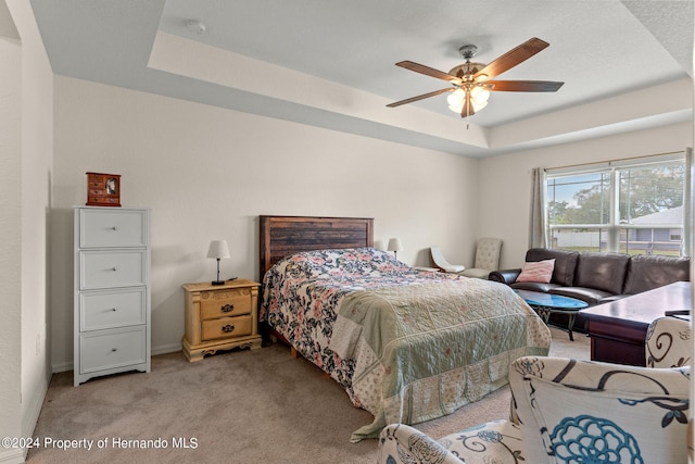 carpeted bedroom with ceiling fan and a raised ceiling