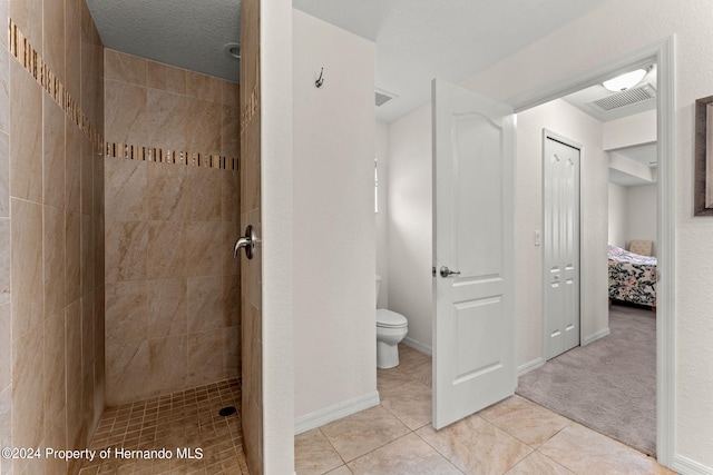 bathroom featuring toilet, a textured ceiling, tile patterned flooring, and tiled shower