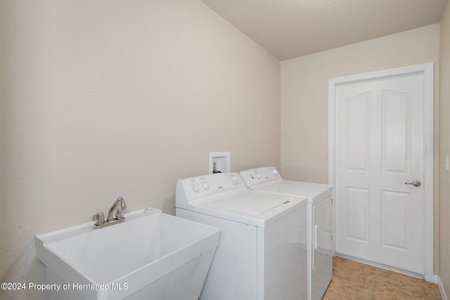 laundry room with washing machine and dryer, sink, light tile patterned flooring, and a textured ceiling