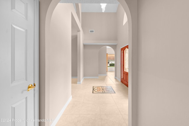 hallway with a towering ceiling and light tile patterned floors