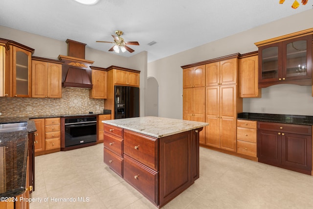 kitchen featuring black appliances, stone countertops, decorative backsplash, ceiling fan, and a center island