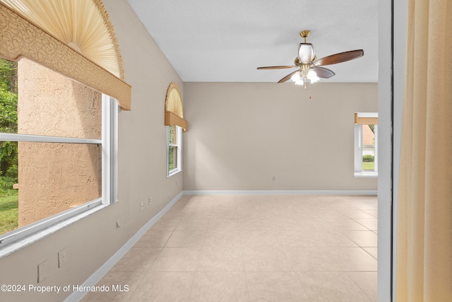 tiled empty room with a wealth of natural light and ceiling fan