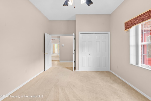 unfurnished bedroom with a closet, light colored carpet, and ceiling fan