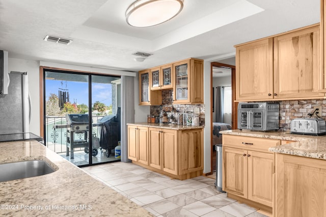 kitchen with a raised ceiling, tasteful backsplash, stainless steel refrigerator, and light stone countertops