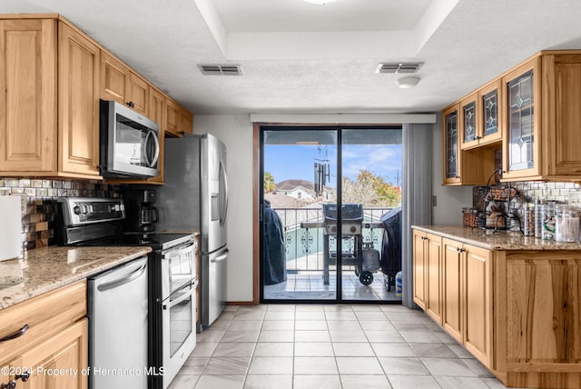 kitchen featuring stainless steel appliances, light tile patterned flooring, tasteful backsplash, light stone countertops, and a textured ceiling