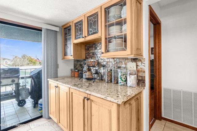 kitchen featuring light tile patterned flooring, light brown cabinetry, backsplash, and light stone counters