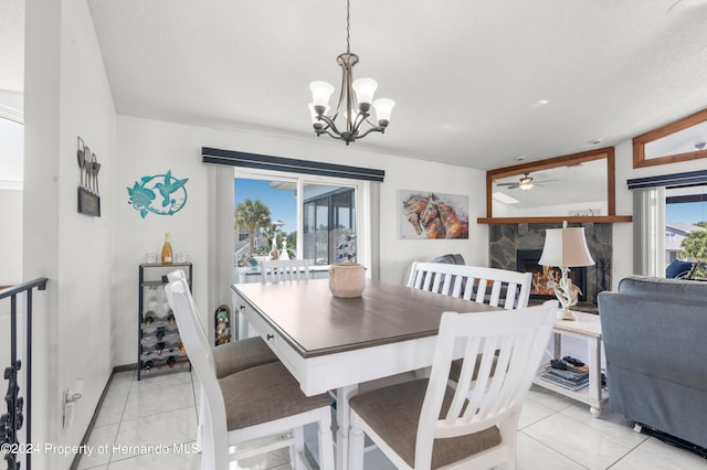 tiled dining space with a fireplace and ceiling fan with notable chandelier