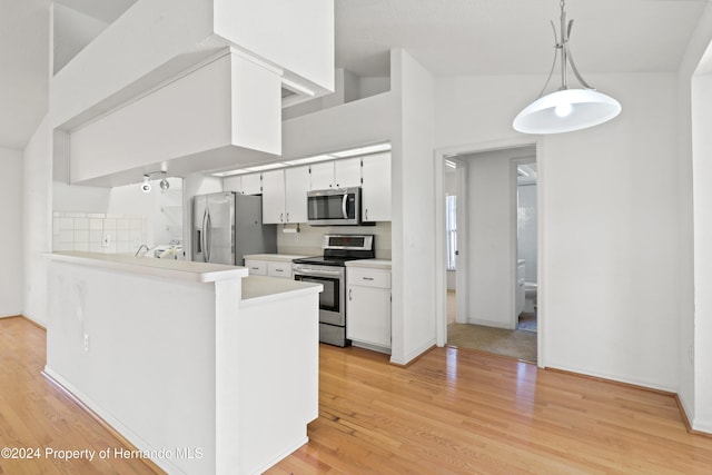 kitchen featuring white cabinetry, kitchen peninsula, appliances with stainless steel finishes, decorative light fixtures, and light wood-type flooring