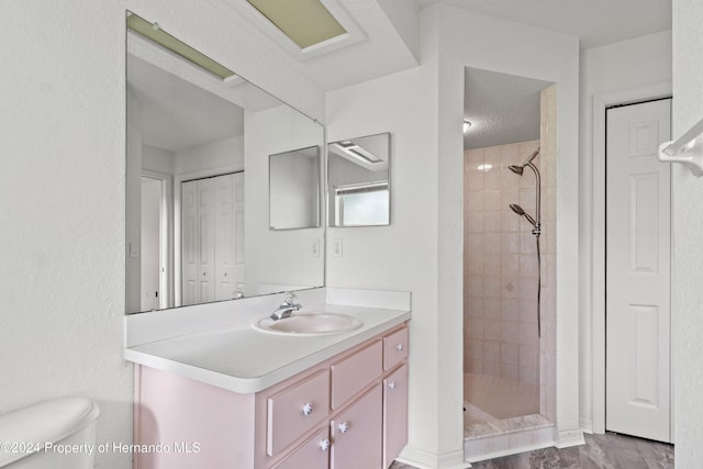 bathroom with vanity, toilet, a textured ceiling, and tiled shower