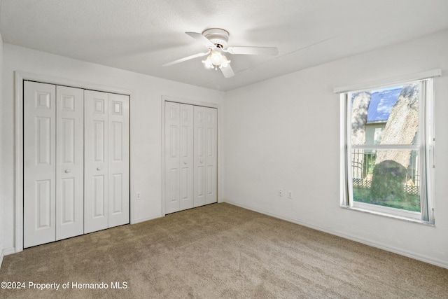 unfurnished bedroom with light carpet, two closets, a textured ceiling, and ceiling fan