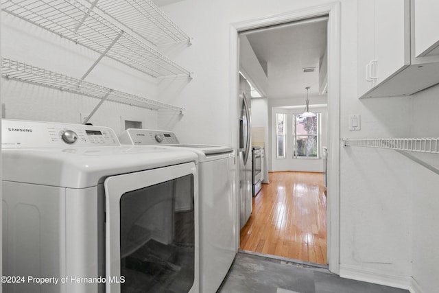 washroom with washing machine and clothes dryer, cabinets, and dark wood-type flooring