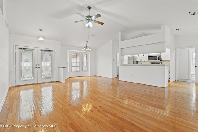 unfurnished living room featuring ceiling fan with notable chandelier, light hardwood / wood-style flooring, high vaulted ceiling, and french doors