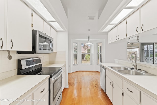 kitchen with appliances with stainless steel finishes, decorative light fixtures, white cabinetry, sink, and light wood-type flooring